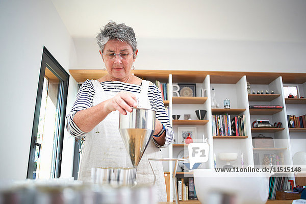 Ältere Frau in der Küche  die mit dem Pfannkuchentrichter Sahne und selbstgemachte Kosmetika in Töpfe abgibt  Mittelteil