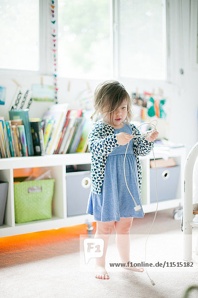 Girl standing in playroom untangling computer cable