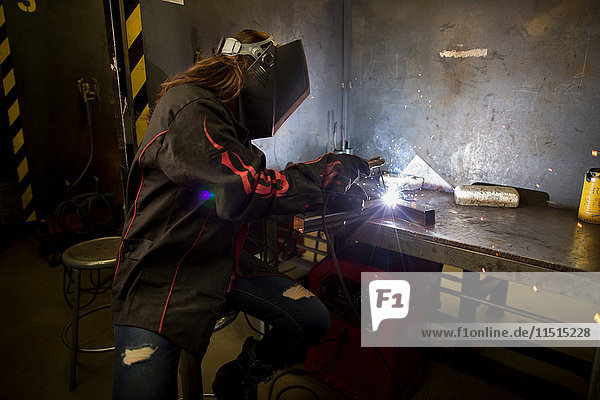 Female metalsmith welding metal at workbench