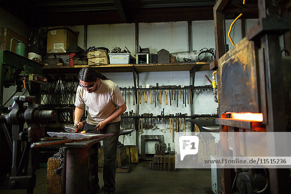 Männlicher Metallschmied hämmert Metall auf Werkstattamboss