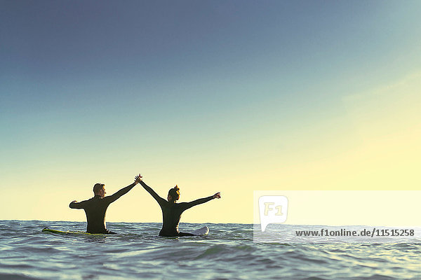 Surfende Paare auf Surfbrettern halten sich im Meer an den Händen  Newport Beach  Kalifornien  USA