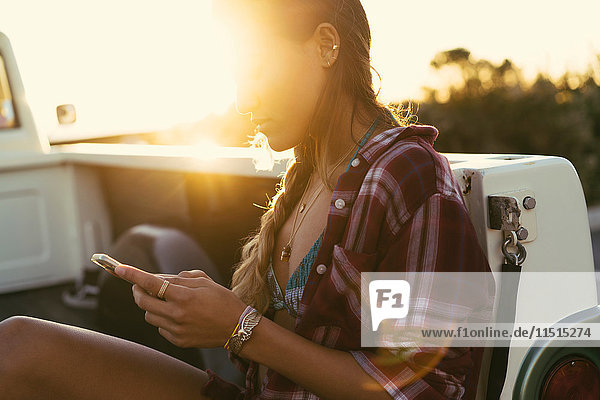 Junge Frau betrachtet ein Smartphone von der Rückseite eines Pickup-Trucks in Newport Beach  Kalifornien  USA