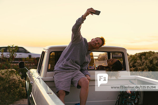 Man taking smartphone selfie with girlfriend in back of pickup truck at Newport Beach  California  USA