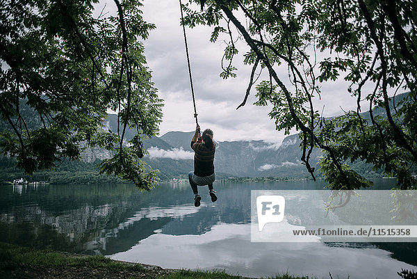 Caucasian woman swinging on rope swing at lake