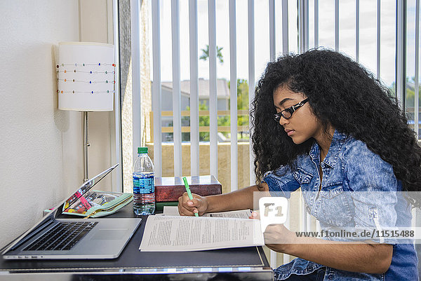Gemischtrassiges Teenager-Mädchen macht Hausaufgaben am Schreibtisch