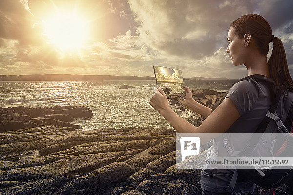 Kaukasische Frau fotografiert Sonnenuntergang am Meer mit digitalem Tablet