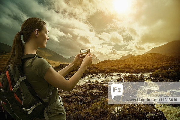 Kaukasische Frau fotografiert Bergfluss mit Mobiltelefon