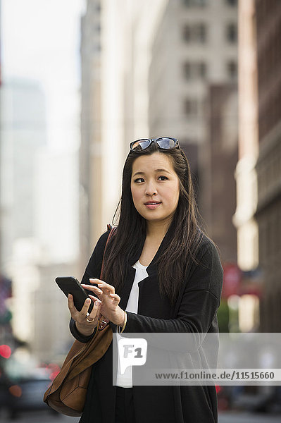 Chinesische Geschäftsfrau  die in der Stadt eine SMS mit ihrem Handy schreibt