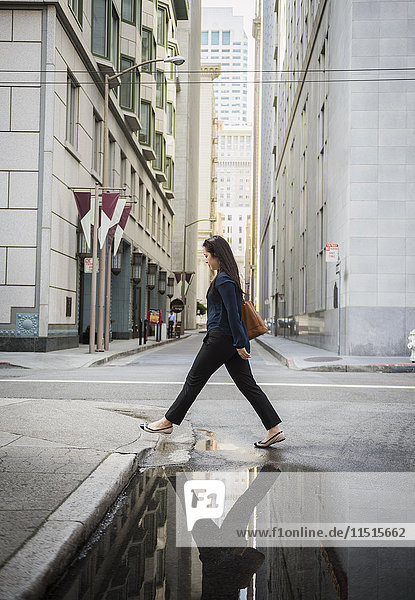 Spiegelung in der Pfütze einer chinesischen Geschäftsfrau  die die Straße überquert