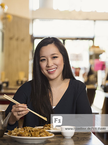 Chinesische Frau isst mit Stäbchen im Restaurant
