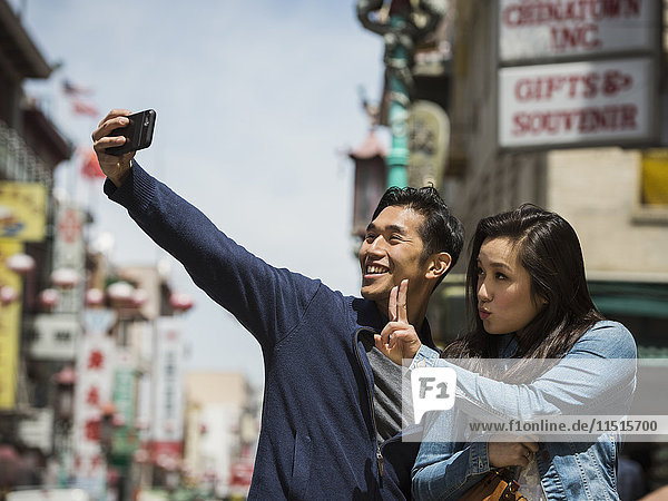Lächelndes chinesisches Paar posiert für Handy-Selfie in der Stadt
