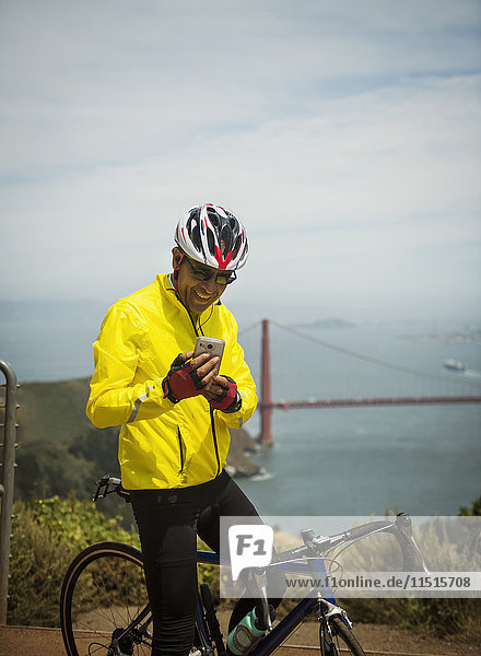 Hispanic man on bicycle texting on cell phone at waterfront