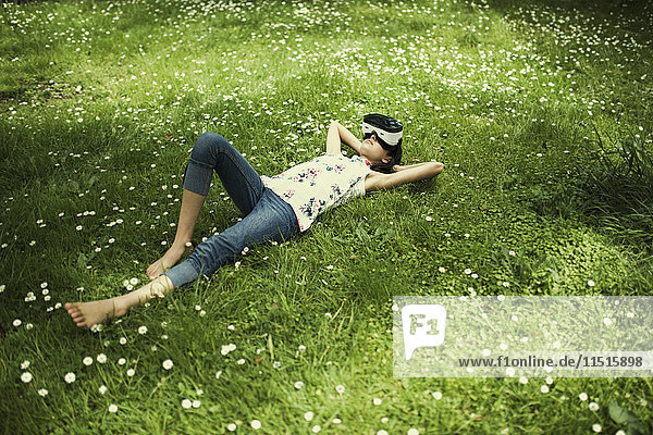 Mixed-Race-Mädchen liegt im Gras und trägt eine Virtual-Reality-Brille