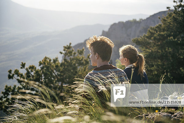 Kaukasisches Paar sitzt auf einem Hügel und bewundert die malerische Aussicht