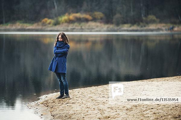 Kaukasische Frau mit blauem Mantel und Schal in der Nähe eines Sees