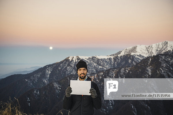 Lächelnder kaukasischer Mann hält leeres Schild in Berglandschaft