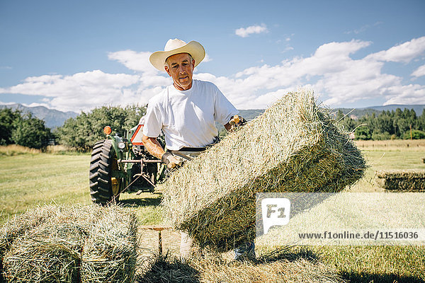 Caucasian farmer in field lifting bale of hay