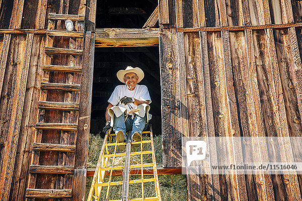 Portrait of smiling Caucasian farmer sitting on ladder in barn