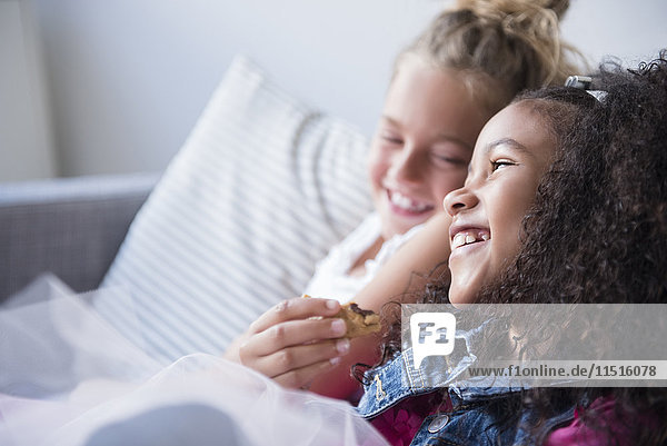 Lächelnde Mädchen essen Kekse auf dem Sofa