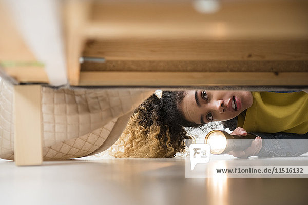 Gemischtrassige Frau sucht mit Taschenlampe unter dem Bett