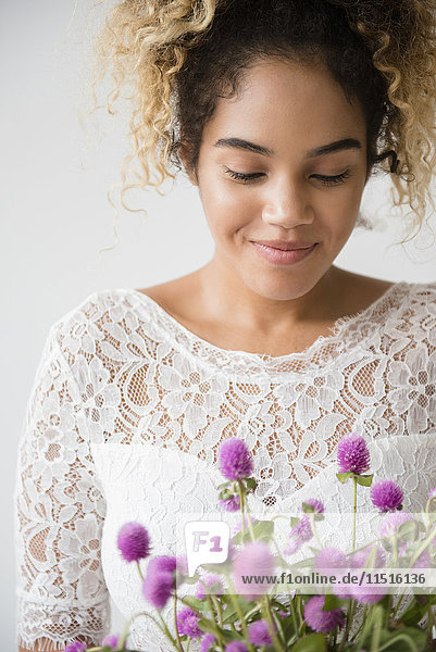 Gemischtrassige Frau im Hochzeitskleid bewundert den Blumenstrauß