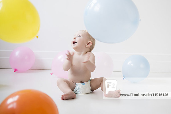 Caucasian baby boy sitting on floor watching balloons