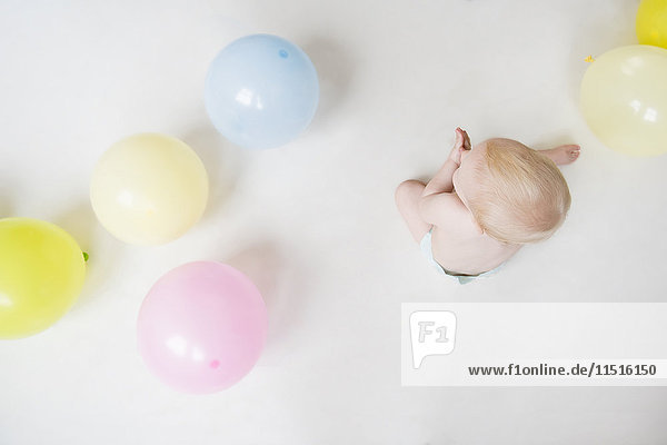 Caucasian baby boy sitting on floor with balloons