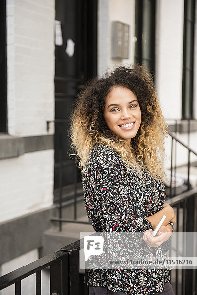 Lächelnde Mixed Race Frau hält Handy in der Stadt