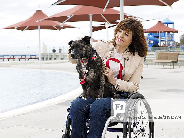 Frau im Rollstuhl sitzend am Wasser mit Hund auf dem Schoß