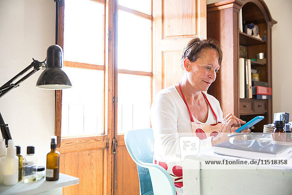 Reife Frau simst auf Büro-Smartphone in handgemachter Seifenwerkstatt
