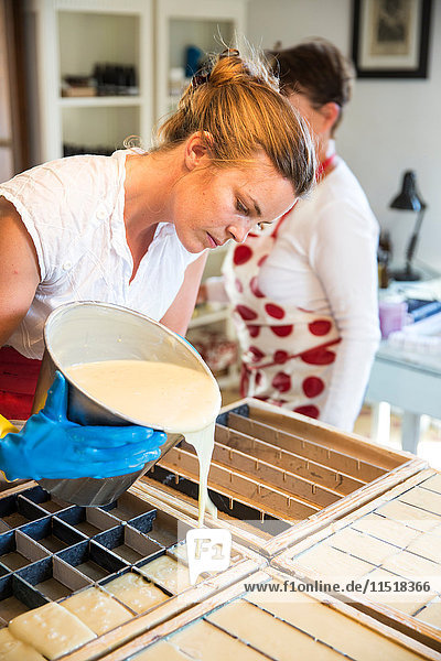 Junge Frau gießt flüssige Lavendelseife in einer Werkstatt für handgemachte Seife in Gussformen