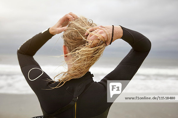 Rückansicht einer Surferin beim Binden nasser blonder Haare am Rockaway Beach  New York  USA