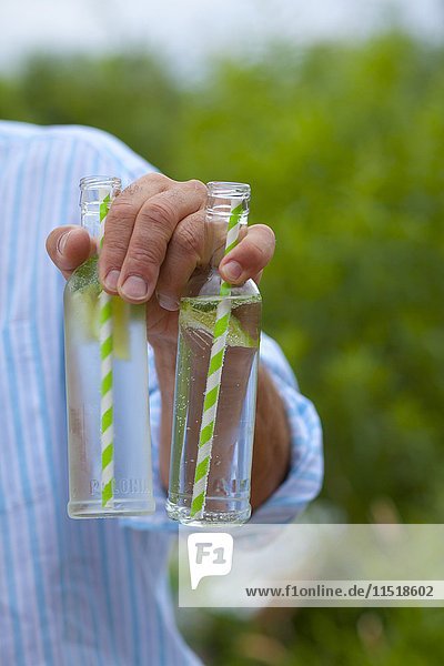 Ein Mann hält zwei jungfräuliche Mojitos in Glasflaschen mit Strohhalmen