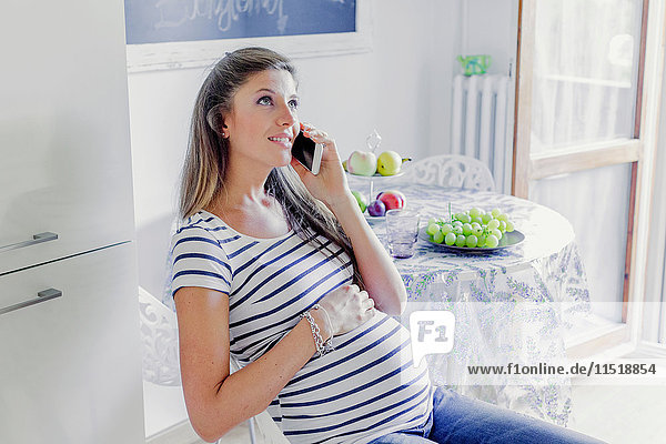 Schwangere Frau telefoniert lächelnd auf Smartphone