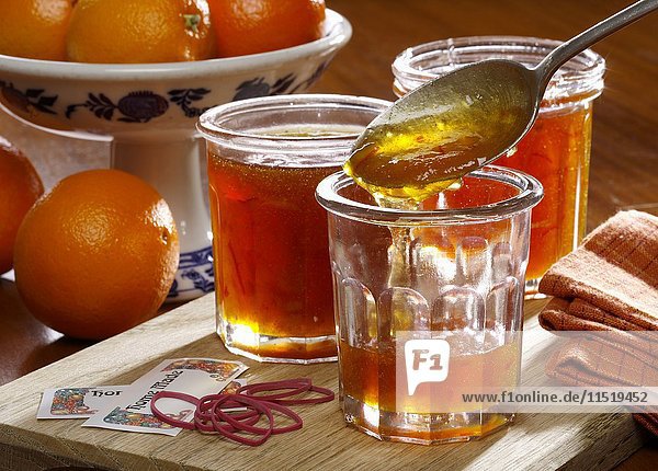 Homemade marmalade being put into jars with whole oranges in the background
