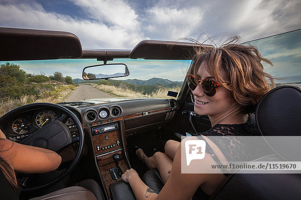 Two young women in convertible car  driving along scenic road  rear view