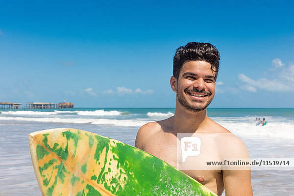 Porträt eines jungen Mannes am Strand  der ein Surfbrett hält  Fortaleza  Ceara  Brasilien