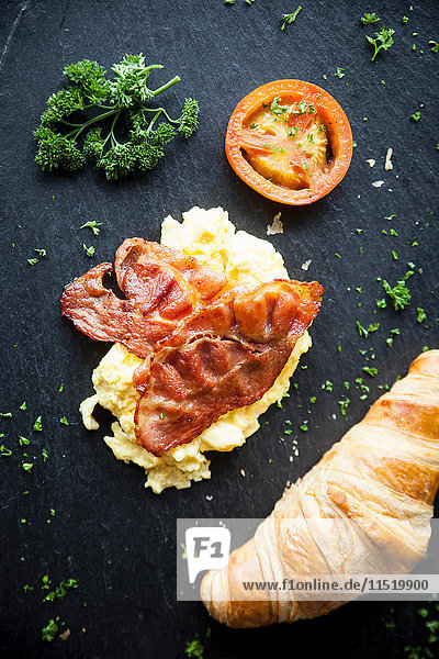 Draufsicht auf Croissant mit Speck,  Omelett und Tomaten Frühstück auf Schiefer