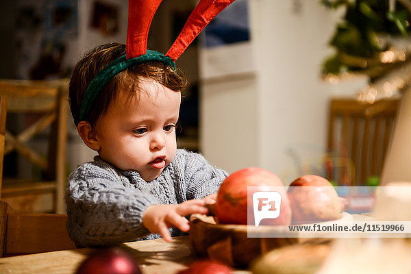 Kleiner Junge mit Weihnachtsgeweih  der Granatäpfel auf dem Tisch anstarrt