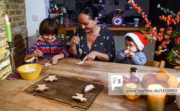 Mutter und zwei Söhne glasieren selbstgebackene Weihnachtsplätzchen am Tisch