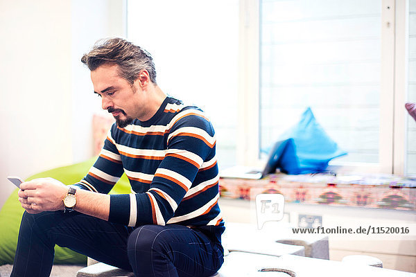 Businessman sitting in office reading smartphone texts