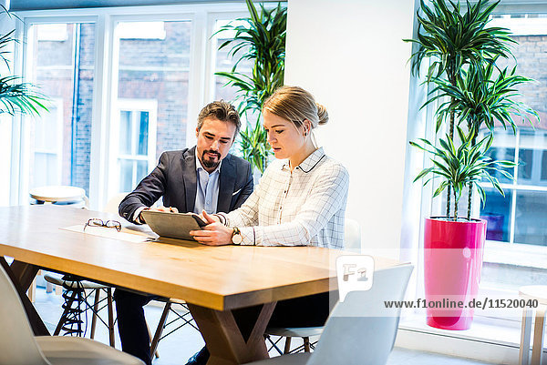 Geschäftsfrau und Mann schauen auf digitales Tablet bei Bürobesprechung