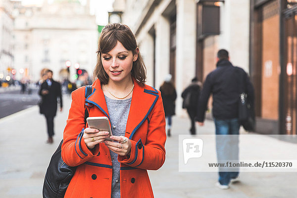 Young woman walking along street using smartphone