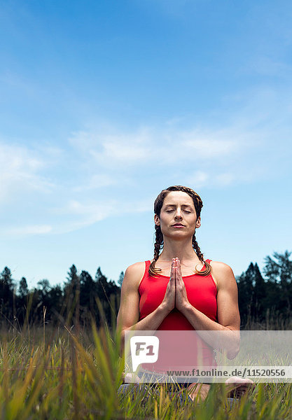 Junge Frau sitzt auf dem Feld  in Yogastellung