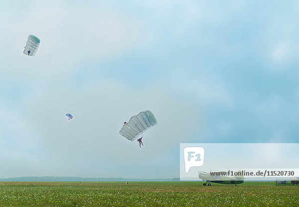 Distanzansicht von drei Personen  die mit einem Oldtimer-Flugzeug mit dem Fallschirm auf einen Flugplatz abspringen