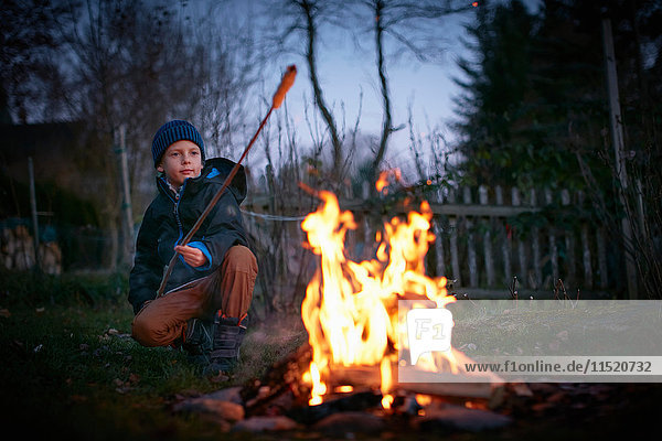 Junge toastet in der Abenddämmerung am Gartenlagerfeuer auf Marshmallows