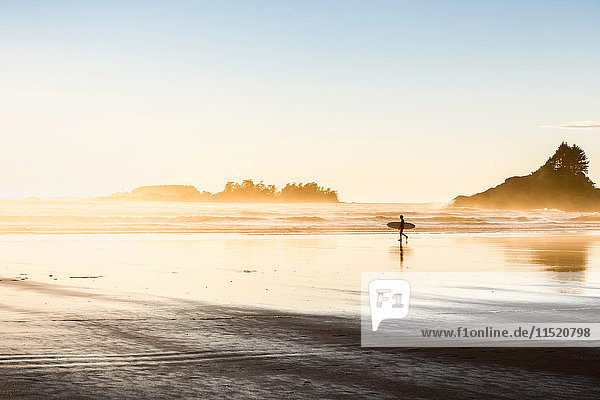 Male surfer carrying surfboard on Long Beach Pacific Rim National Park Vancouver Island British Columbia Canada