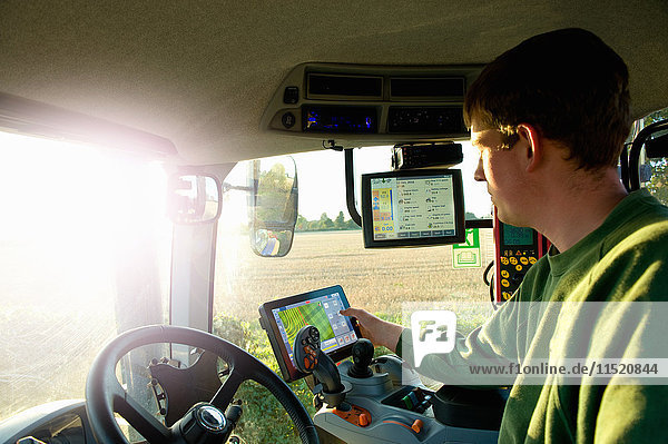 Junger Mann fährt Traktor mit Touchscreen am globalen Positionierungssystem