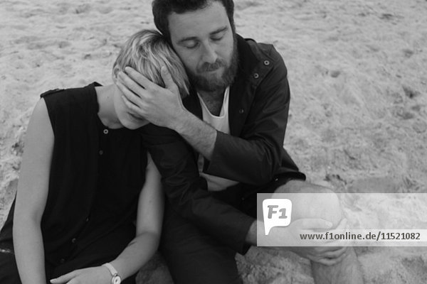 Junges Paar sitzt am Strand und entspannt sich ineinander