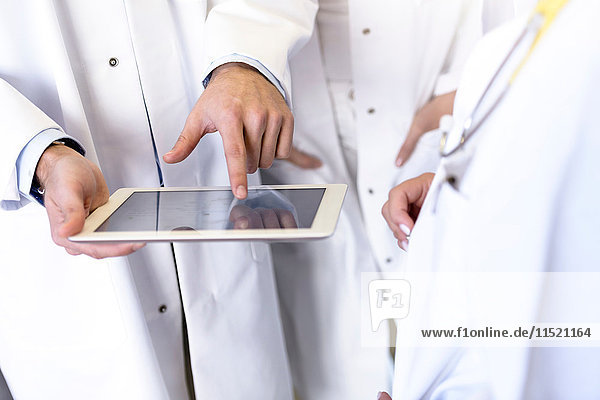 Mittlere Sektion männlicher und weiblicher Ärzte  die im Krankenhaus einen Touchscreen mit Digitalpad verwenden